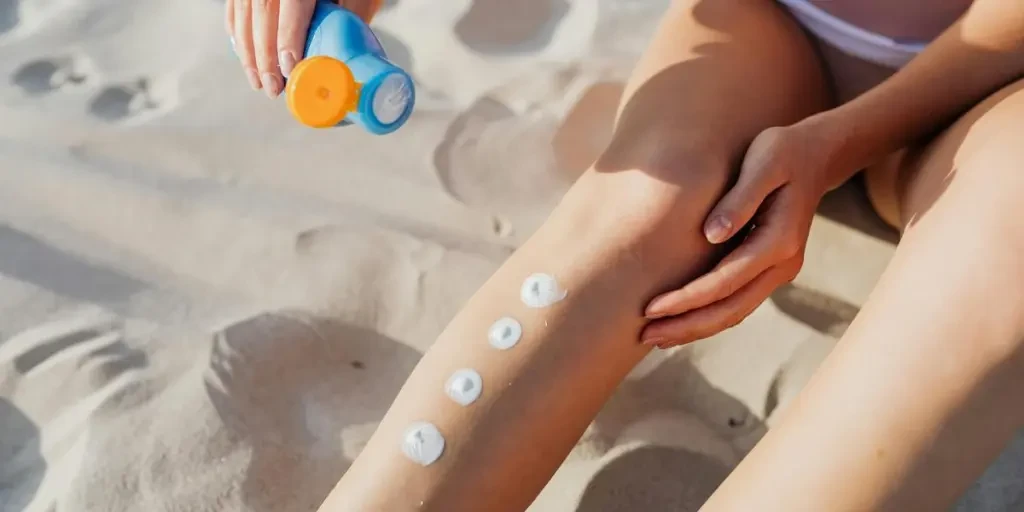 Close-up of applying sunscreen on legs at the beach for skin protection