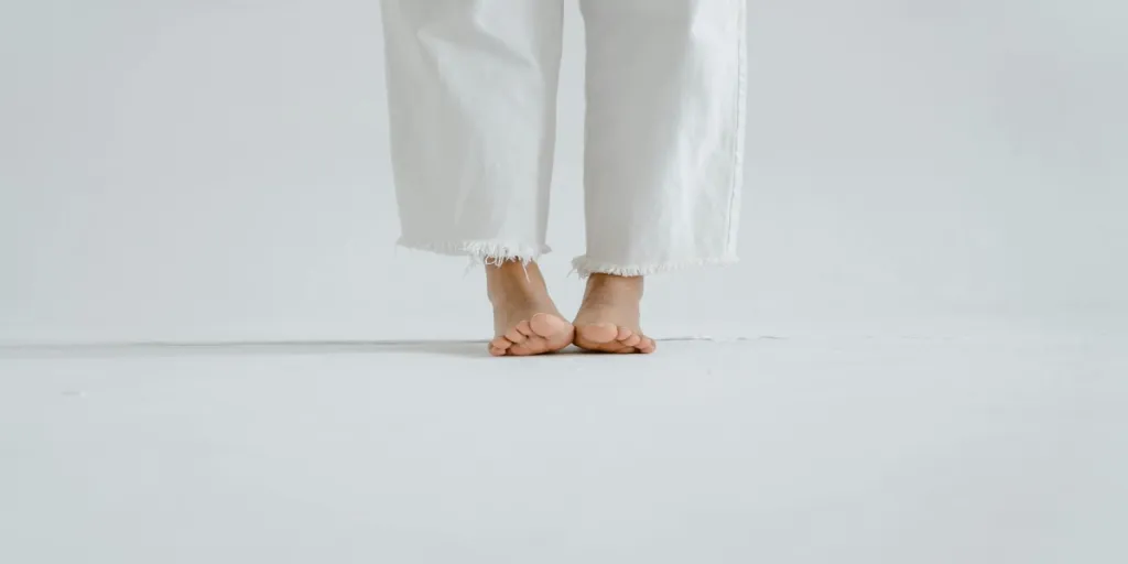 Close-up of bare feet in white jeans on a white minimalist background by Tima Miroshnichenko