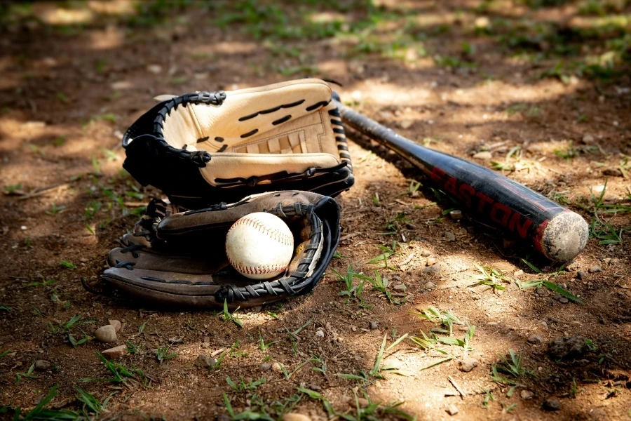 Close-up of baseball equipment including ball, bat, and gloves on a rural dirt ground