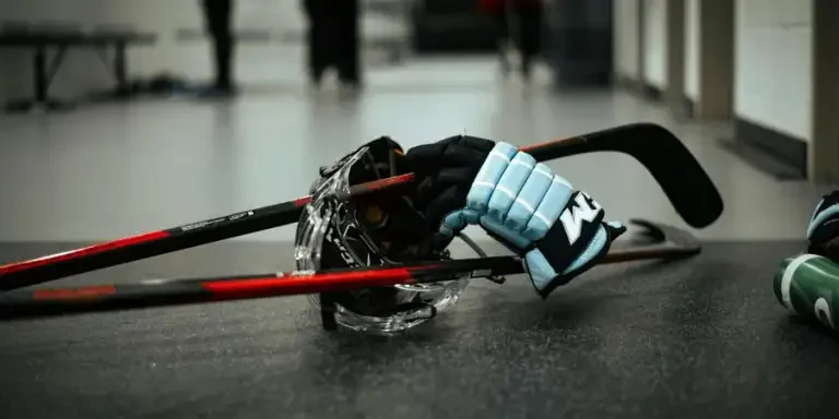 Close-up of hockey gloves, helmet, and sticks on an indoor ice rink floor, conveying sports readiness