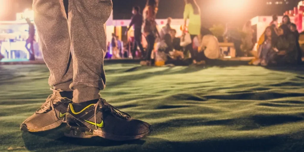 Close-up of sneakers with a blurred group in the background at a night festival