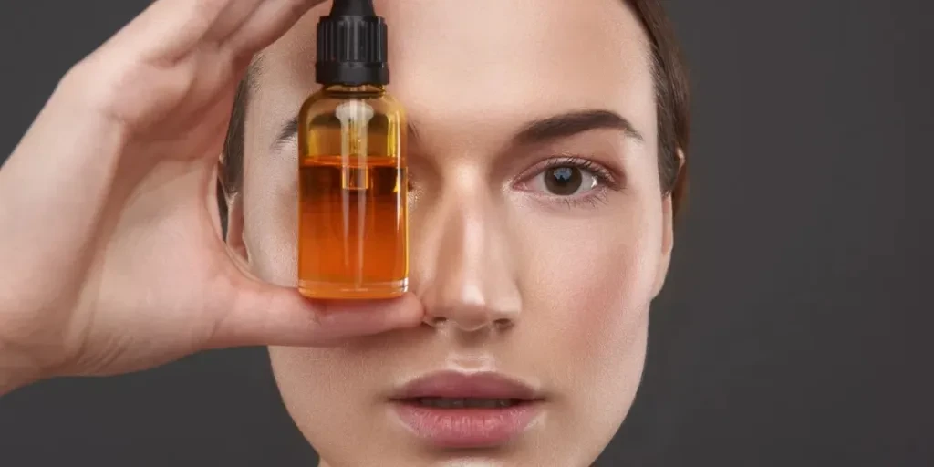 Close up portrait of smiling lady holding bottle of orange serum and making funny face