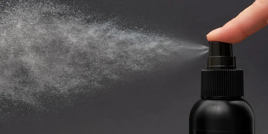 Close-up view of human hand and black spray bottle isolated on black