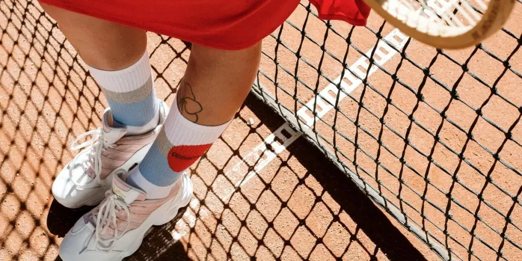 Close-up view of tennis player’s feet on a clay court, highlighting white sneakers and colorful socks