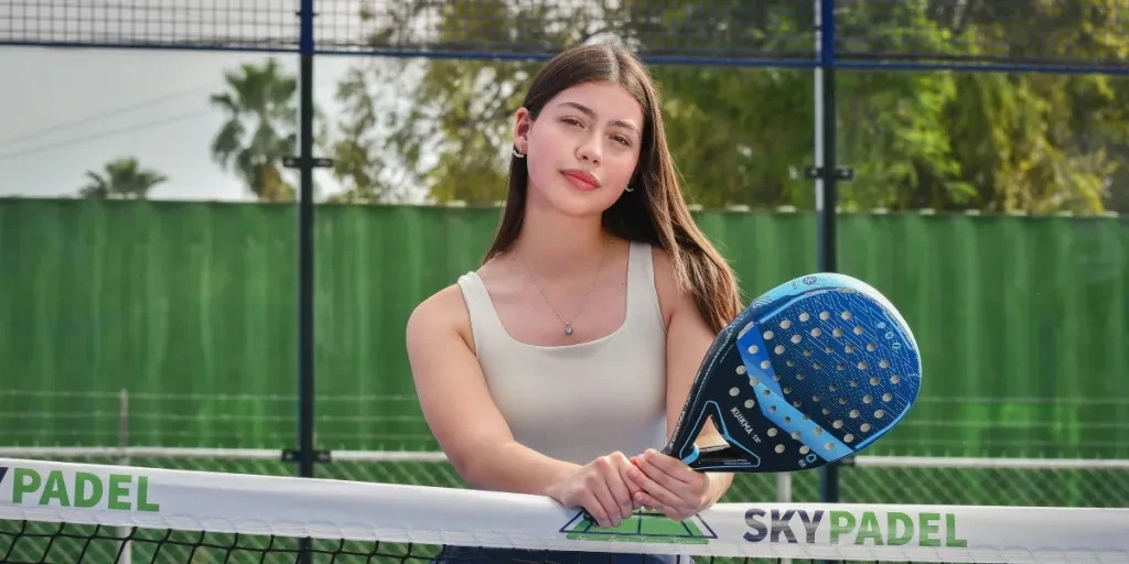 Confident woman holding a padel racket, standing on an outdoor court. Perfect for sports and lifestyle themes