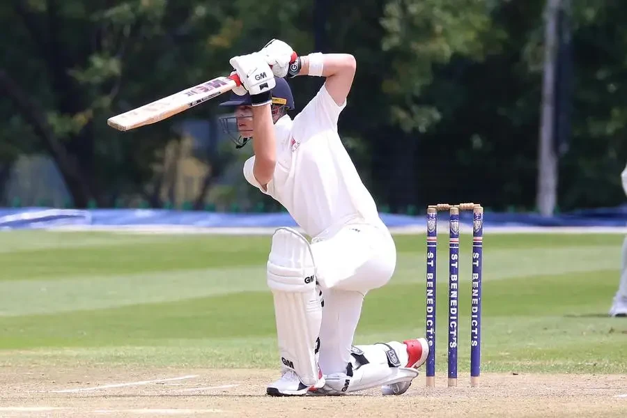 Cricketer in action performing a sweep shot on a sunny outdoor pitch