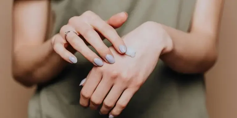 Crop anonymous female in casual shirt with manicured hands and ring softly rubbing hand moisturizer in back of hand skin