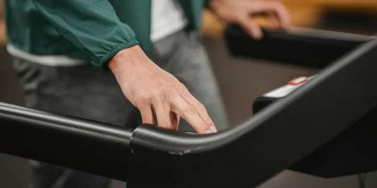 Crop anonymous male in activewear checking speed and time of treadmill on blurred background