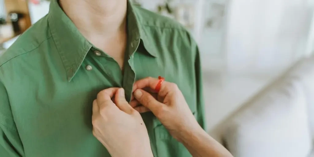 Detail shot of someone buttoning a green shirt, reflecting care and style