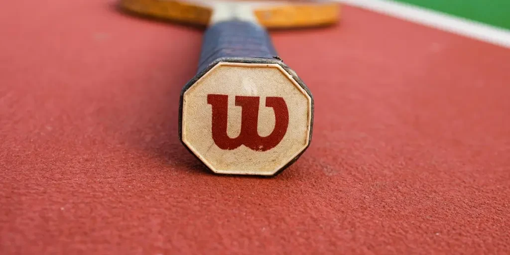 Detailed close-up of a tennis racket on a vibrant red tennis court surface