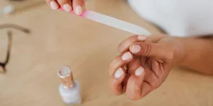 Detailed view of hands filing nails with a nail polish bottle nearby, showcasing personal grooming by Photo