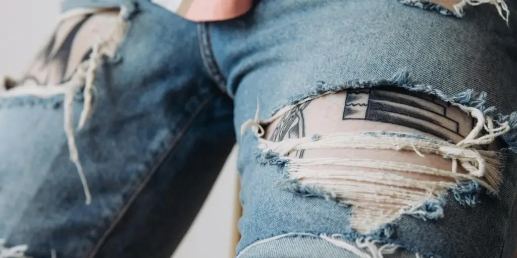 Detailed view of worn denim shorts with tattoos peeking through, showcasing unique style