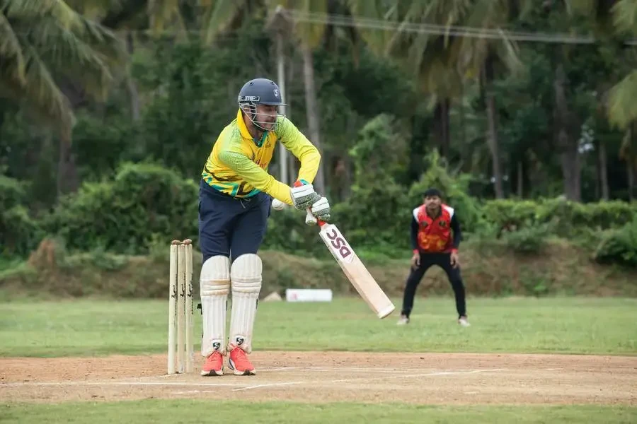 Dynamic cricket action shot with batsman in colorful gear and fielder in vibrant outfit on lush green field