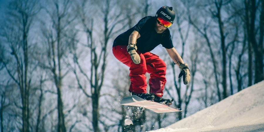 Dynamic snowboarder catching air on a snowy slope surrounded by bare trees. Capturing the thrill of winter sports