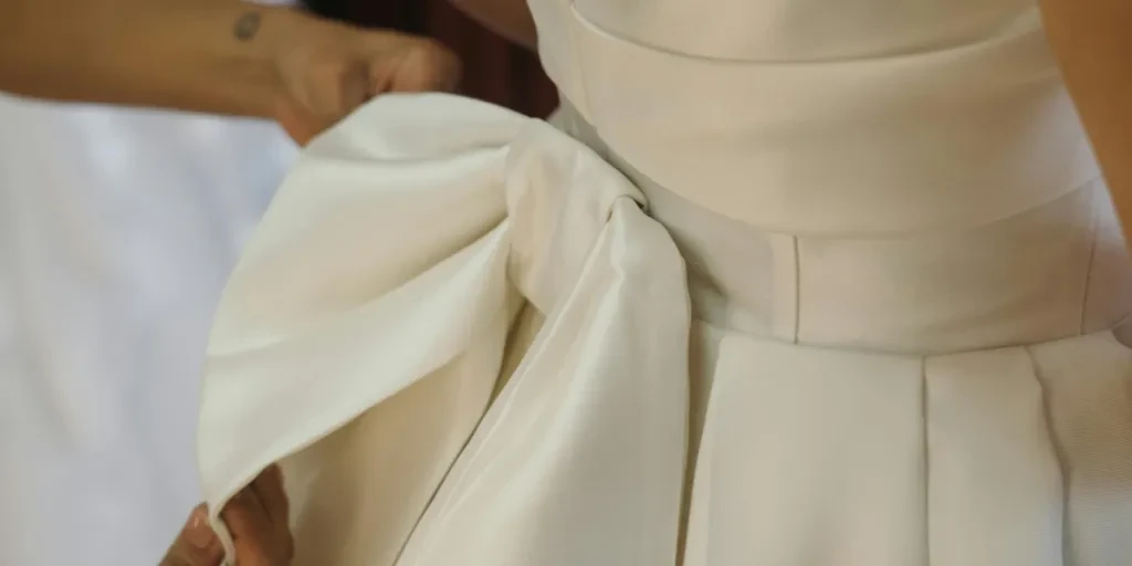 Elegant close-up of a white bridal dress bow being adjusted during a wedding preparation