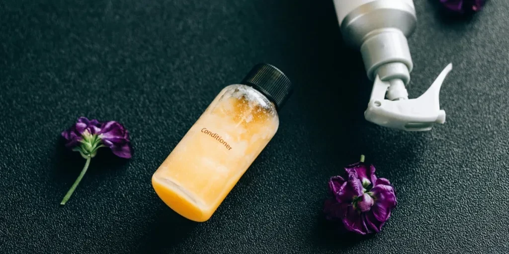 Elegant flat lay of conditioner and spray bottle with vibrant purple flowers on dark background