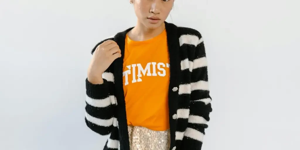 Fashionable young girl posing in striped cardigan and orange shirt