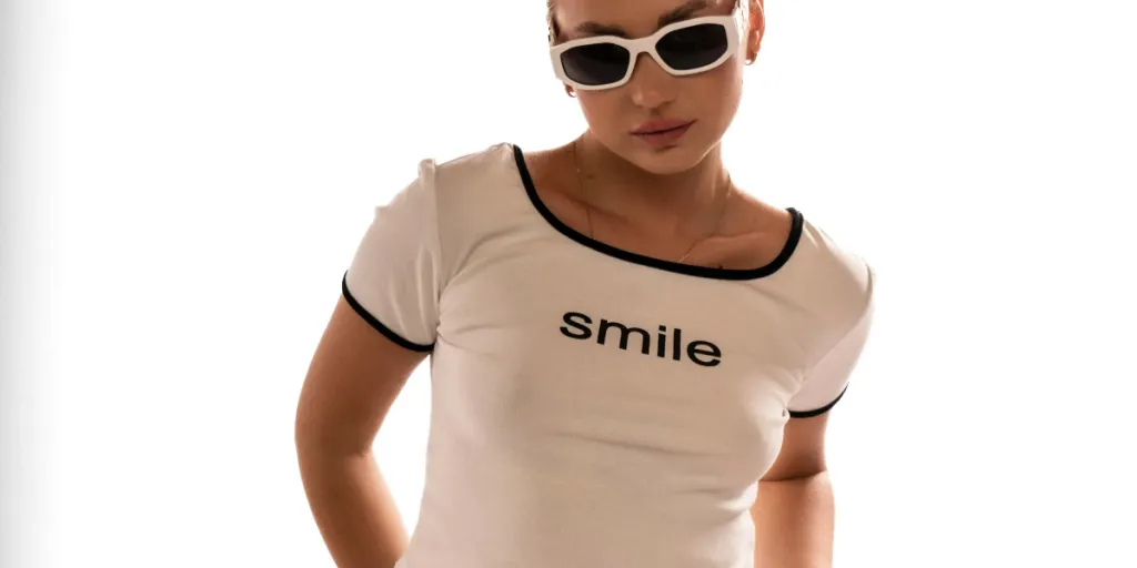 Fashionable young woman wearing sunglasses and a smile t-shirt poses with confidence by Katia Miasoed