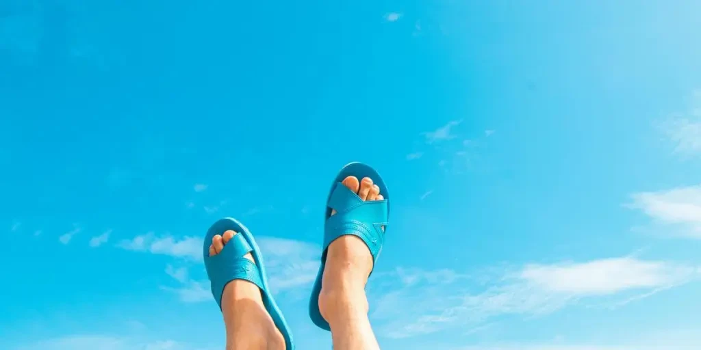 Feet in blue sandals against a clear summer sky, embodying relaxation