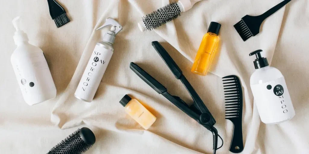 Flat lay image of various hair care products and tools on a textured fabric surface