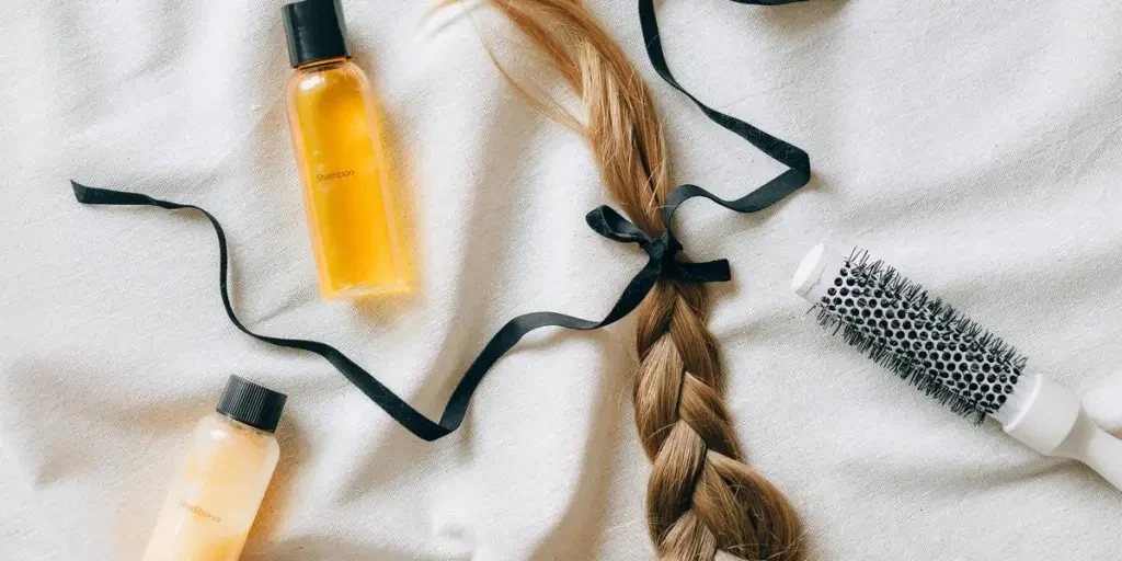 Flat lay of braided hair with shampoo bottles and brush on white fabric, conveying beauty and haircare themes