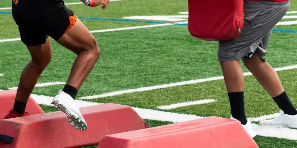 Football player running sideways over barriers about to take a hit from his coach