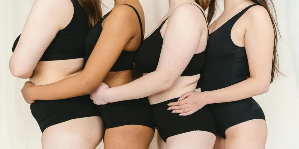 Four diverse women in black underwear hugging, promoting body positivity and inclusivity