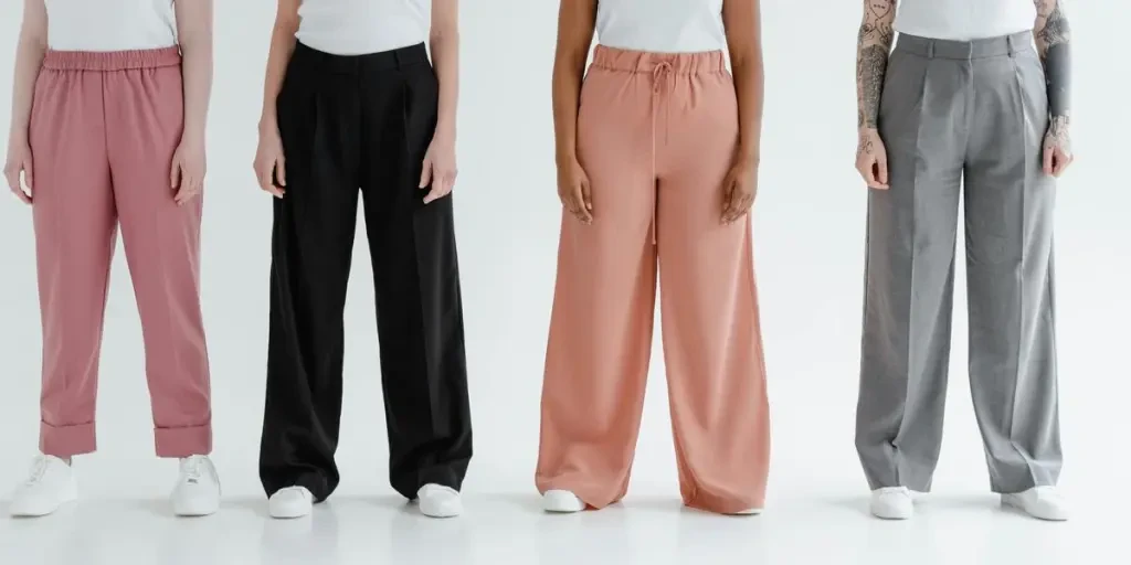 Four women stand in colorful trousers against a white background, showcasing diversity and fashion