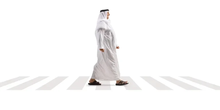 Full length profile shot of an arab man in a white thobe and headscarf walking over a pedestrian crossing isolated on white background