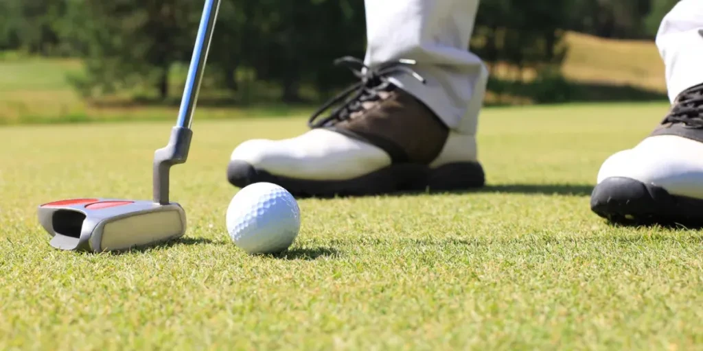 Golf player at the putting green hitting ball into a hole