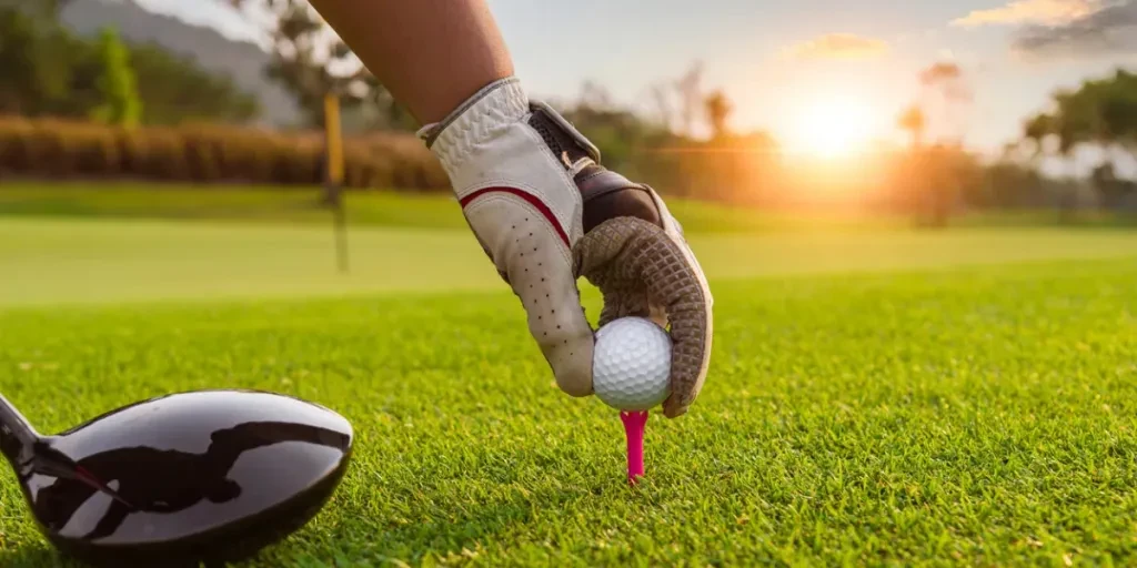 Golfer hold golf ball put on tee by black and white glove with sunlight ray blur green golf course background