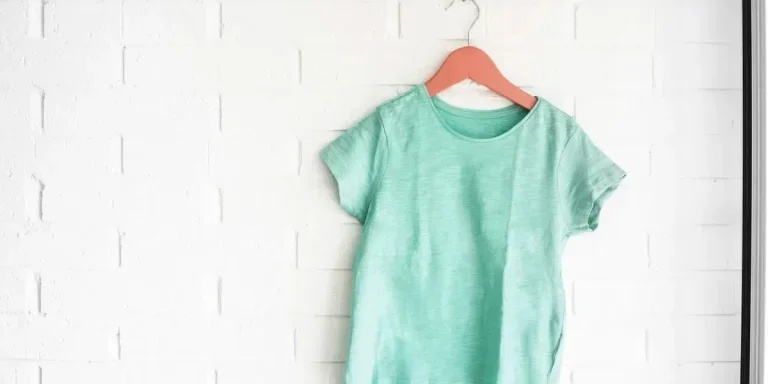 Green tshirt hanging on an orange hanger in a white wall