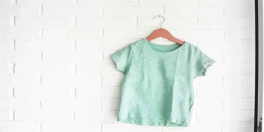 Green tshirt hanging on an orange hanger in a white wall