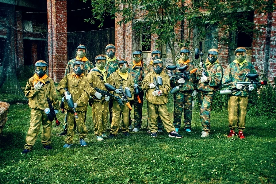 Group of paintball players wearing camouflage gear and masks, holding paintball guns outdoors