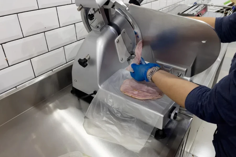 Hands of a shop assistant wearing disposable plastic gloves using ham slicer machine