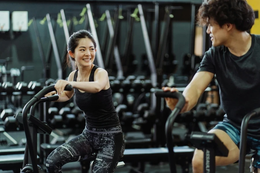 Happy Asian couple working out on elliptical trainers in a gym