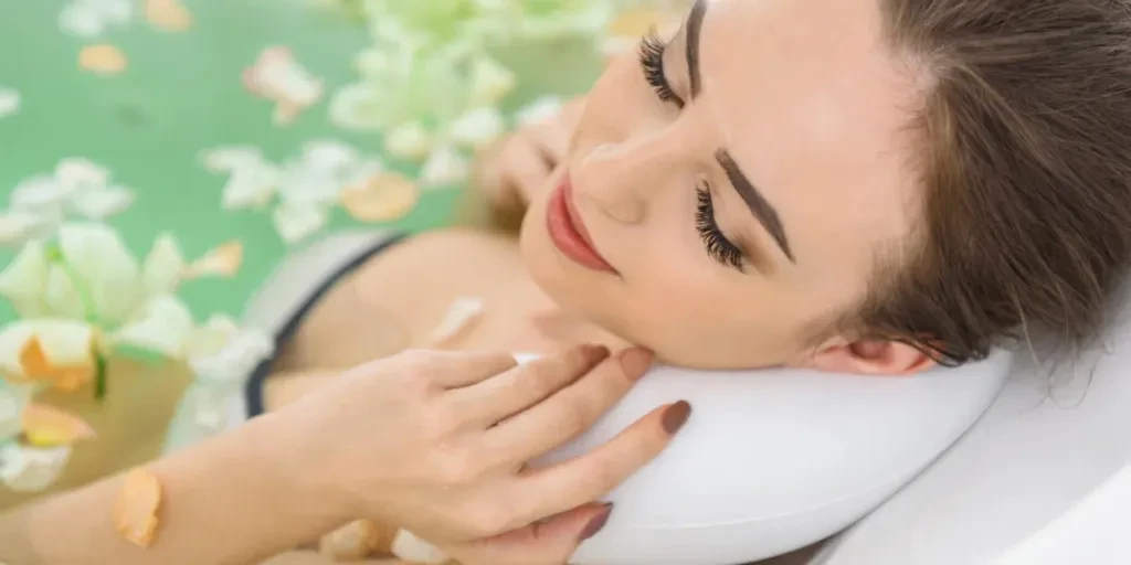 Happy young girl is lying in bath with petals