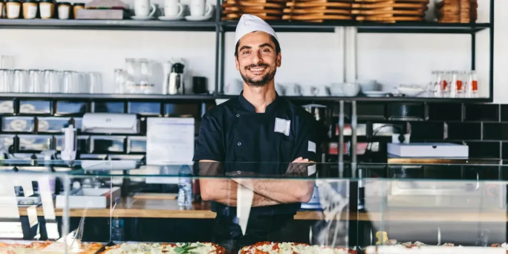 Italian chef or pizzaiolo with sicilian pizza in restaurant smiling portrait