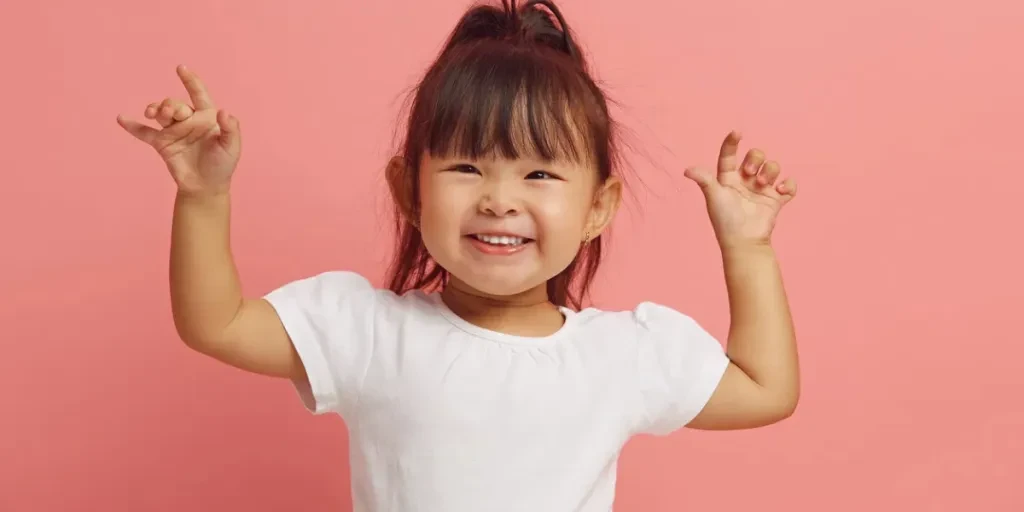 Joyful three years old Asian ethnicity little girl raises her hands up