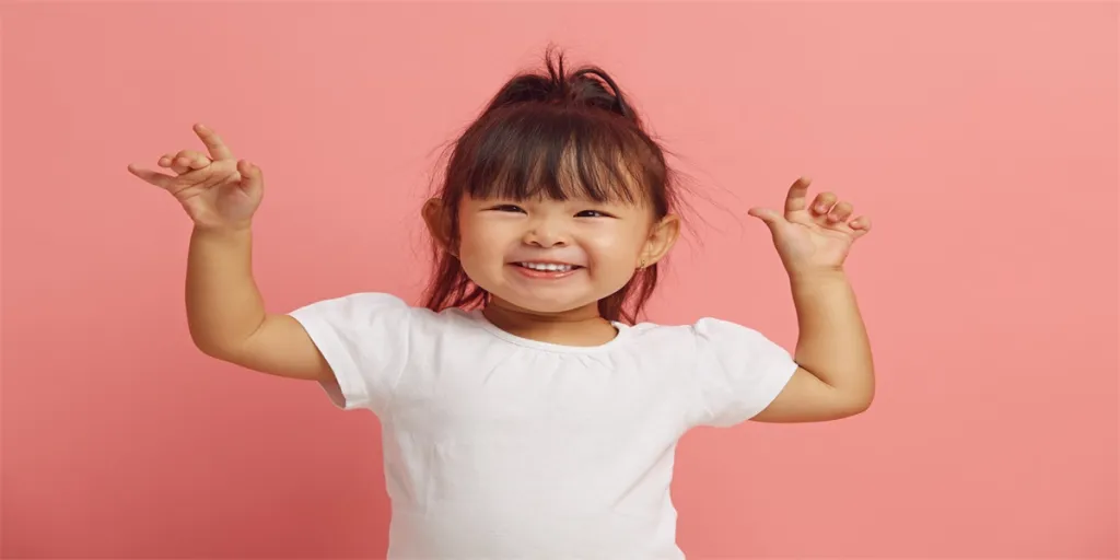 Joyful three years old Asian ethnicity little girl raises her hands up