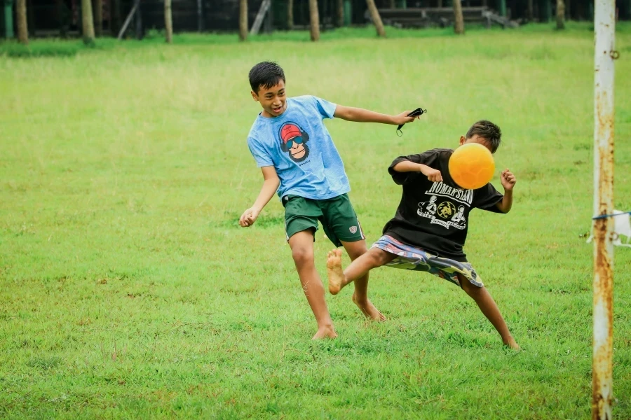 Kids play soccer barefoot in the grass field