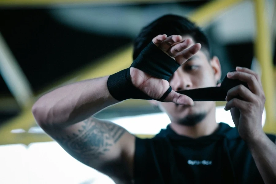 Male Asian athlete bandaging hands with elastic dark wraps before boxing workout in gym