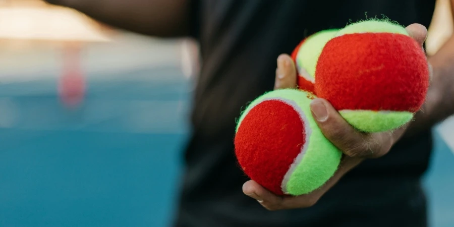 Man holding three practice tennis balls on tennis court