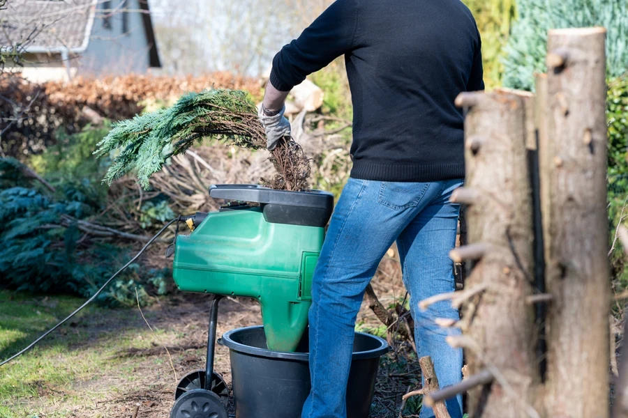 Man inserting small tree branches into an electric shredder