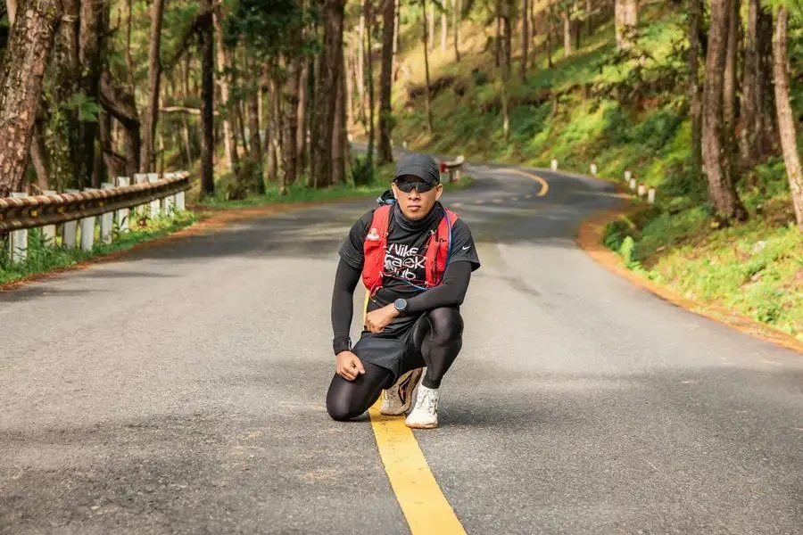 Man kneels on a winding road in Đà Lạt forest, embodying fitness and adventure by Tuong Chopper