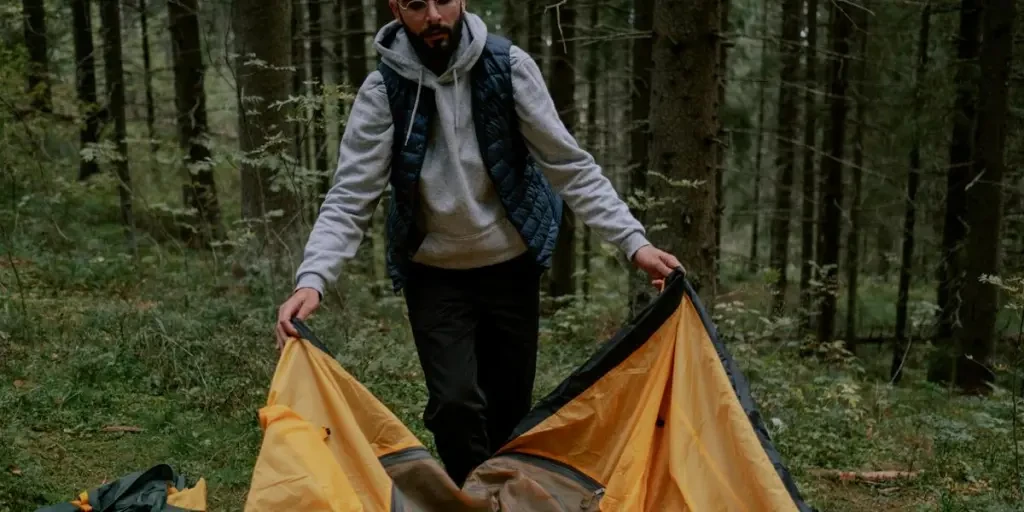 Man setting up a yellow tent in the forest, preparing for camping adventure