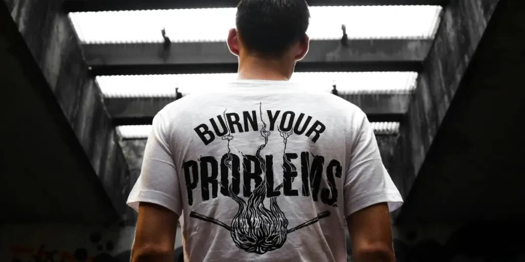 Man standing indoors, wearing a t-shirt with Burn Your Problems text, viewed from behind