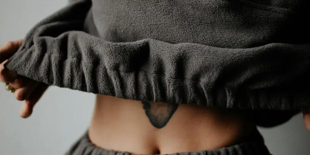 Midsection of a woman in charcoal attire showcasing a tattooed belly. Fashionable and artistic depiction