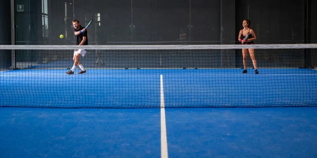 Mixed padel match in a blue grass padel court indoor behind the net