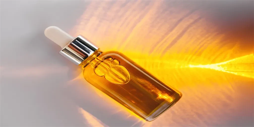 Mockup of glass dropper bottle with a metal cap and yellow essential oil on a background with an abstract fire pattern of light and shadow